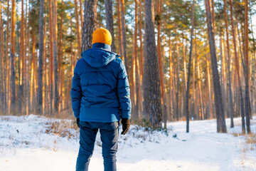 Fototapeta na wymiar Rear view of young man in yellow hat on the background of a snowy landscape in a winter pine forest