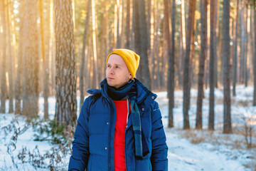 Young man in winter yellow hat walks in winter snowy pine forest