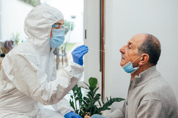 Health Professional in PPE suit and face shield introducing a nasal swab to a senior adult patient...