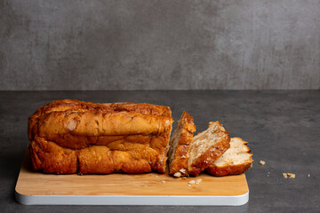 Partly sliced colorful orange brown Sugarloaf bread on a wooden cutting board contrasted against a clean minimalist contemporary fashionable rustic gray kitchen with sugar parts laying around