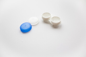 An open white container for lenses next to lie the lids on the white background 