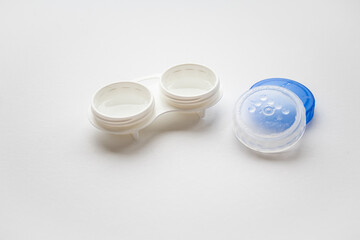 An open white container for lenses next to lie the lids 