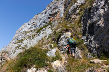 Hombre joven senderista subiendo por unas cadenas de hierro en la ruta de anillo de picos en el parque nacional de los picos de europa dirigiendose a collado jermososo.