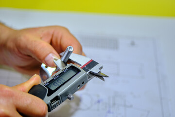 A man hand measuring the M8 bolt bonding fastener by means of calliper with blurred technical drawing and yellow background.