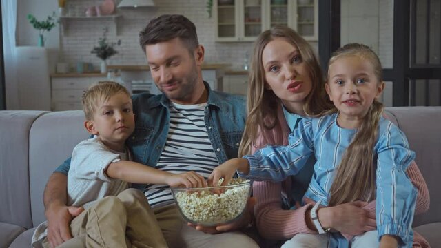 Family with popcorn talking while looking at camera at home