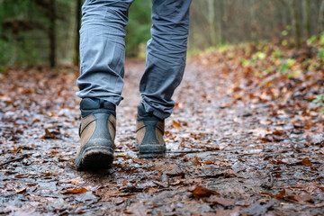 Close up of hiker walking down the wet forest path. Person with dirty hiking shoes on the footpath outdoors.