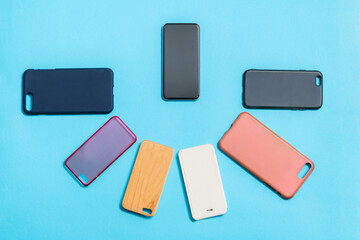 Pile of multicolored plastic back covers for mobile phones on blue background with a phone on the side