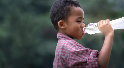 Closeup portrait of dark-skinned boy drinks water from a bottle on green park, blur nature...