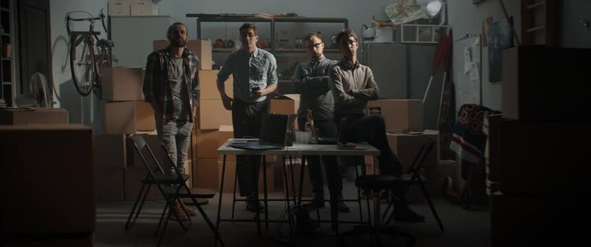 WIDE Team of young entrepreneurs posing and looking into camera. Launching their small IT business startup company from garage. Shot with 2x anamorphic lens