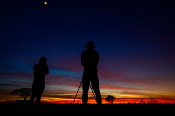 Fototapeta premium Silhouette of couple photographer standing on open field at sunset background.