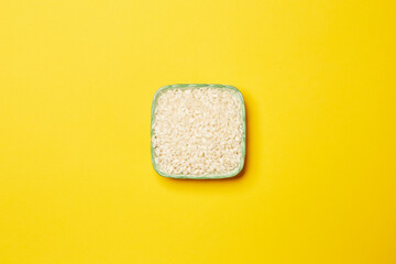 Top view of uncooked white rice in the square shaped green ceramic bowl isolated on the yellow background