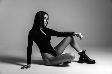 Photoshoot of a young brunette. A girl in a black bodysuit and black shoes. Fitness exercises. Black and white photo.