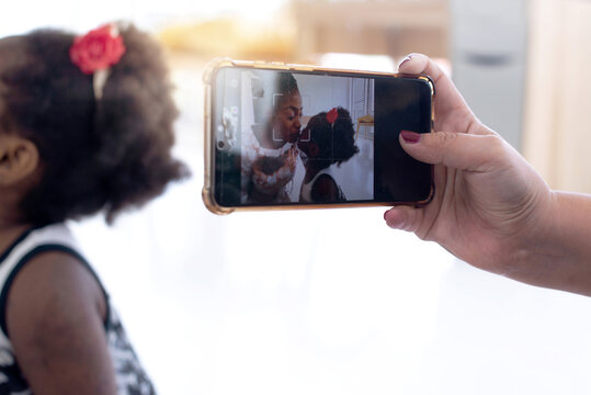 Woman's hand taking a picture of mother and daughter with  smartphone, image of African mother and child girl are showing love by kissing