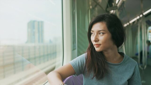 Cute asian woman travel by sky train in Thailand undeground. Teen girl looking at window of metro train. Concept of public transport and urban journey
