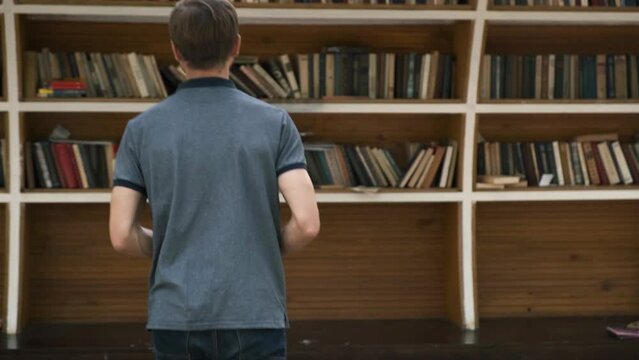 Young bearded millennial man reding book on city bookcrossing station. College student at street library book exchange point, free public bookcase.