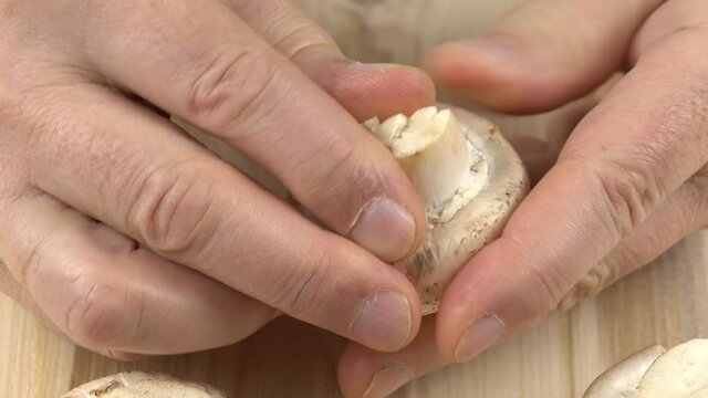 Man prepares mushrooms for cooking, separating the caps from the stipes.