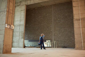 Wide angle view of female construction worker wearing hardhat while standing in big concrete archway, copy space