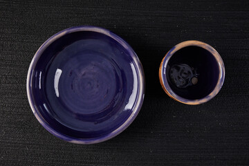 Blue clay ceramic cup and plate on the black background, top view