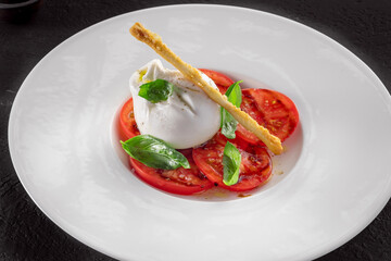 Burrata cheese and tomato salad with Basil and olive oil on a dark background