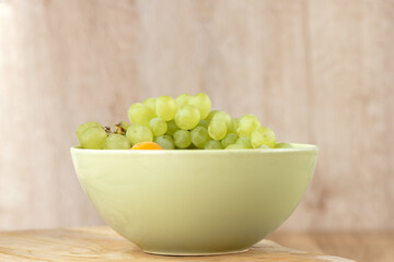A bunch of green grapes in a deep bowl stands on a wooden table