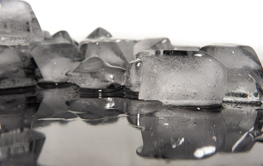 Ice cubes melting on dark reflective surface, white background, selective focus.