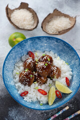 Blue bowl with asian style rice and meatballs in teriyaki sauce, vertical shot on a dark grey stone background