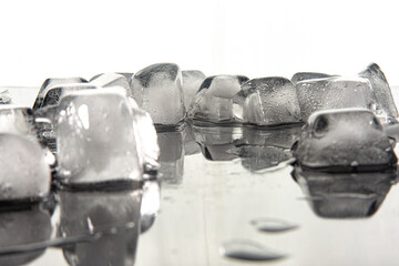 Ice cubes melting on dark reflective surface, white background, selective focus.
