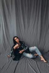 Obraz premium Photoshoot of a young brunette. Girl in jeans. Grey background.