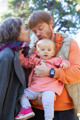 Cute couple of parents and little daughter posing outdoors. Mom and dad holding cute baby girl in arms, standing in autumn park. Vertical shot. Family portrait concept