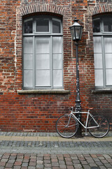 Fototapeta na wymiar White bicycle tied to a streetlamp in front of a brick wall
