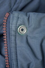 one white metal rivet on a gray garment fabric with a brown plastic zip