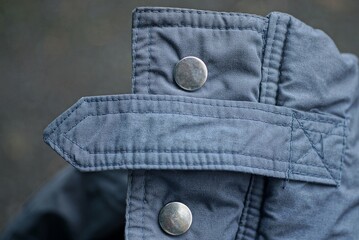 two metal buttons, rivets and a long harness on the gray fabric of the jacket