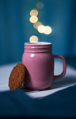 Pink cup of warm tea with ginger cookie on the blue background with blurred lights