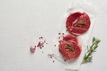 Two fresh Parisienne raw steak on white parchment paper with salt, pepper and rosmary in a rustic style on old wooden background. Black angus. Top view.