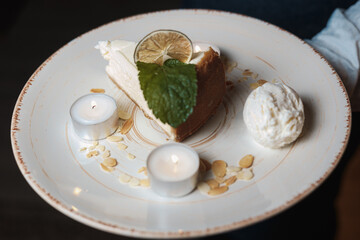 A piece of cheesecake served with ice cream ball with candles on a white plate