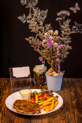 Grilled steak with french fries and vegetables served on a wooden table.
