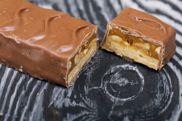 Chopped up chocolate bar. Filled with caramel and nuts. On black pine boards.