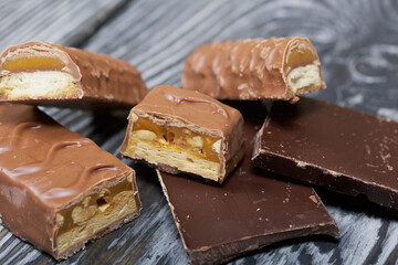 Chopped up chocolate bar. Filled with caramel and nuts. Nearby are pieces of chocolate. On black pine boards.