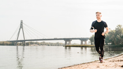 Young fit male runner jogging near the river bank in summer