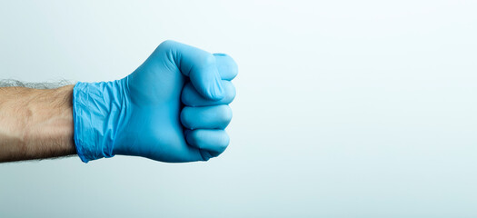 A fist in a medical glove. Doctor's hand in a blue medical glove on a light background.