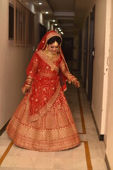 Obraz premium Young Indian Bride in her traditional wedding dress smiling and posing for photographs. She is not looking directly towards the camera