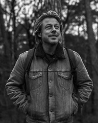 Obraz premium Happy man in jeans jacket with backpack in forest. Black and white photo.