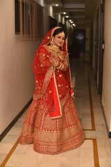 Young Indian Bride in her traditional wedding dress smiling and posing for photographs. She is not looking directly towards the camera