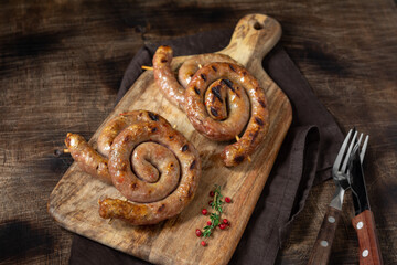 Spiral grilled sausages on a serving Board on a brown wooden table. Spiral sausages. Homemade meat...