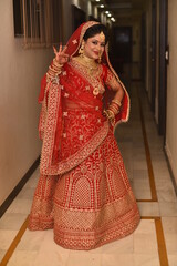 Young Indian Bride in her traditional wedding dress smiling and posing for photographs. She is not looking directly towards the camera