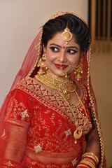 Young Indian Bride in her traditional wedding dress smiling and posing for photographs. She is traditional red color lehenga 
