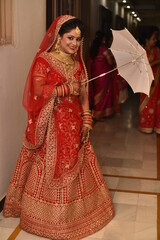 Cute Indian bride in her traditional wedding dress which is red designer lehenga posing for...