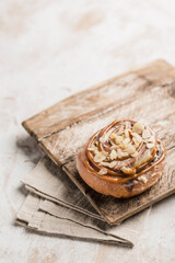 Bun Cinnabon with caramel and almond slices on wooden Board with a napkin on a light background.
