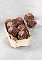 Cocoa muffins sprinkled with powdered sugar in a wooden box on a light gray background