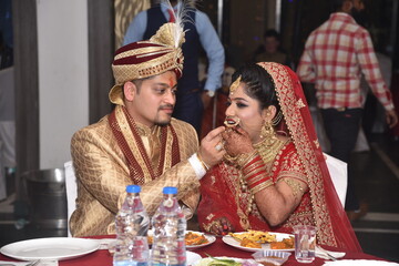 Bride groom having food during wedding ceremony. Both  are wearing traditional Indian wedding dress and groom is helping bride by offering her food 